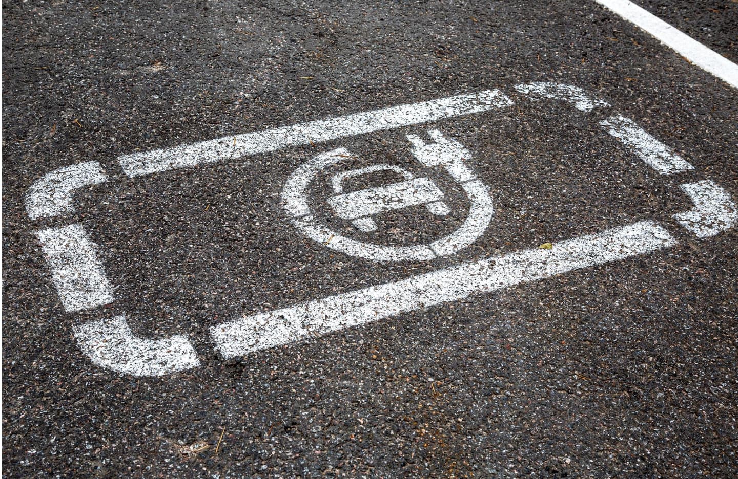 Handicapped parking space symbol painted on asphalt near commercial EV charging stations.