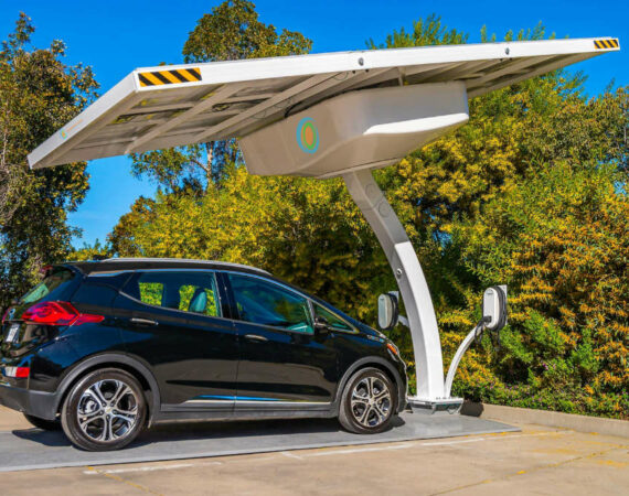 An electric car is parked and charging under a solar panel canopy at an Arizona commercial EV charging station.