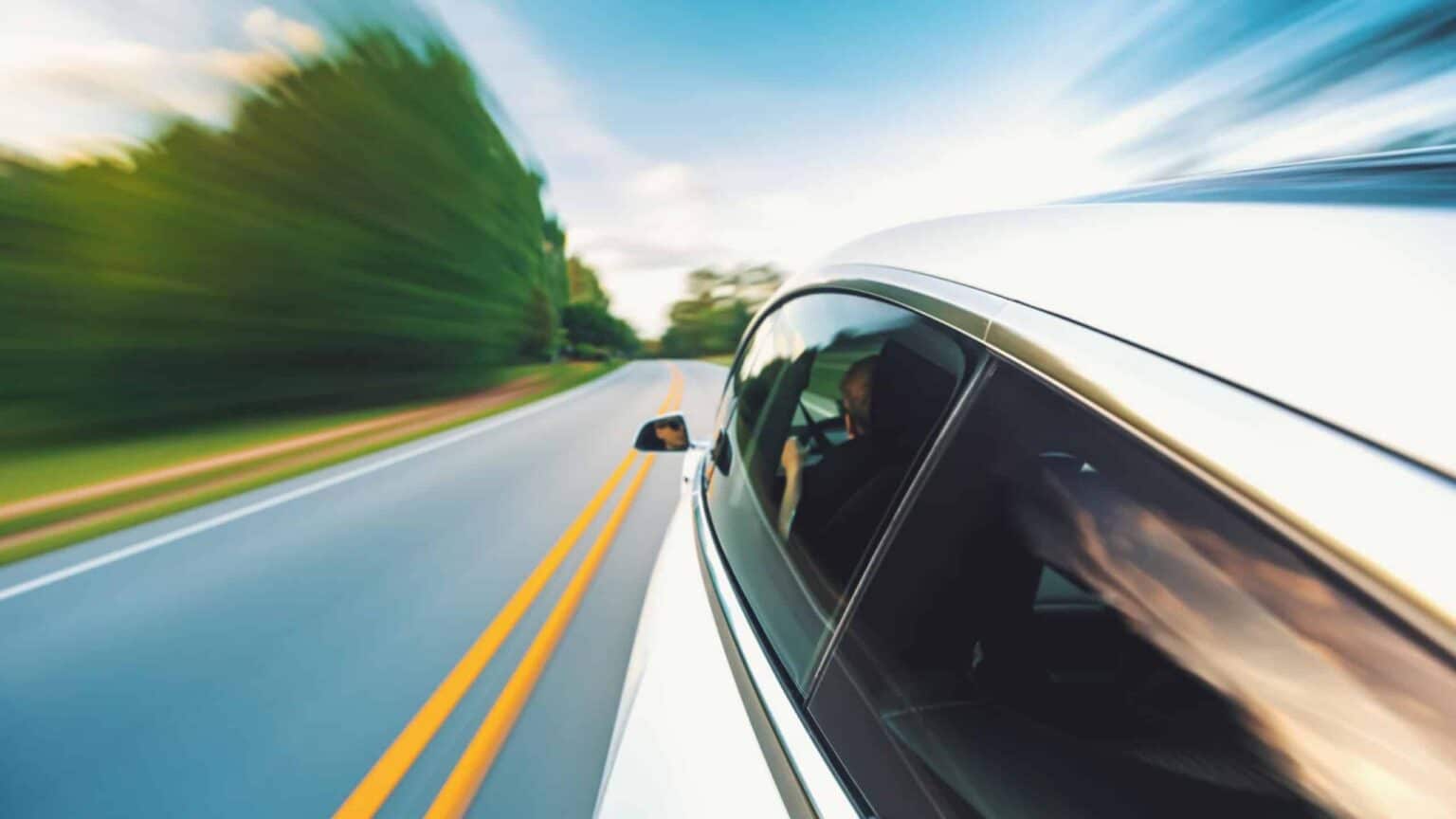Silver car driving at high speed on a curved road with motion blur.
