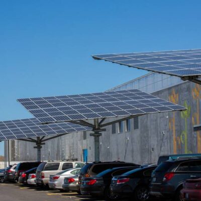 Solar panel-covered parking with a commercial EV charging station and a wind turbine in the background on a clear day in Arizona.