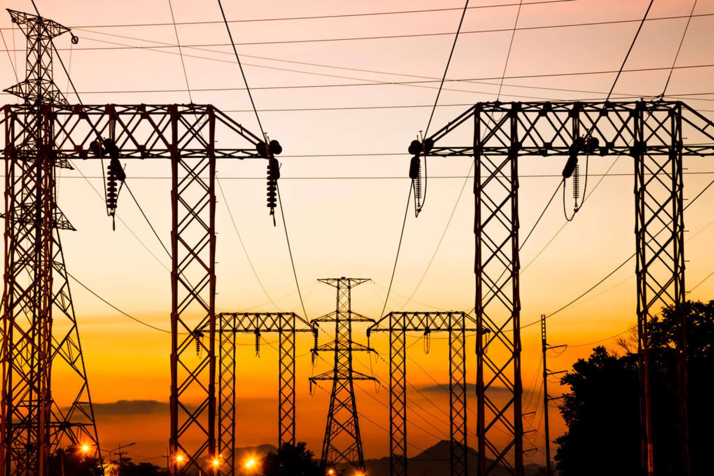 Electricity pylons, integral to Vehicle to Grid Charging, silhouetted against a sunset sky.