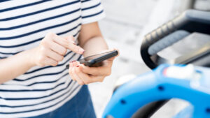 Woman using a smartphone near a baby stroller, browsing California ZEV Vehicle Sales 2022.