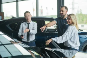 Car salesperson showing a vehicle to a couple in a dealership showroom.
