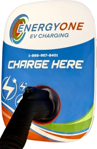 An EnergyOne Level 2 EV charging station labeled "EnergyOne EV Charging" with a phone number and the words "CHARGE HERE" displayed prominently.
