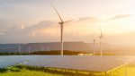 Renewables on the rise: Wind turbines and solar panels grace a green landscape under a clear sky, with the sun setting in the background, reflecting 2024's key highlights in energy generation data.