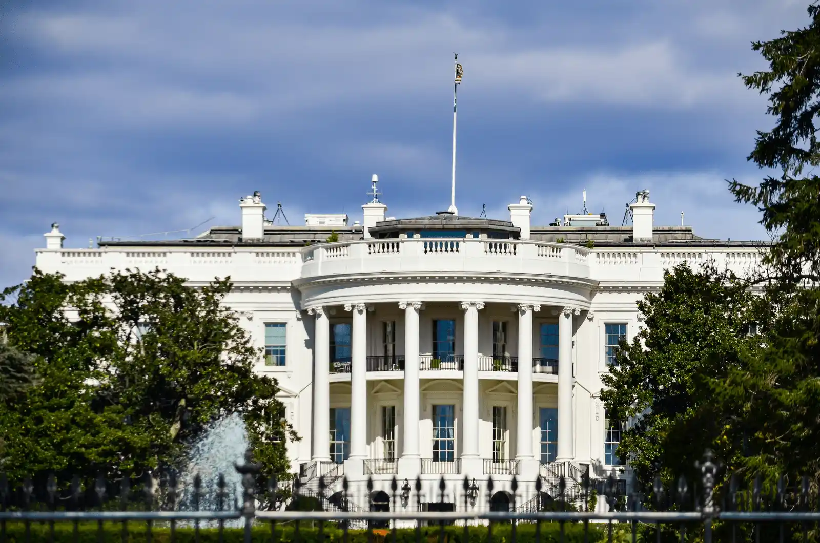 The White House, with its circular balcony and surrounded by trees under a cloudy sky, stands as a backdrop to the ongoing lobbying efforts in Washington to maintain clean energy tax credits for businesses.