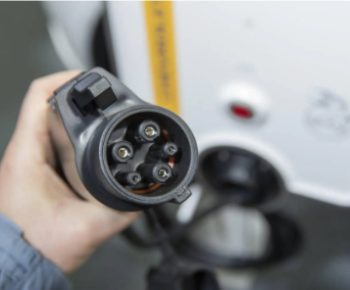 Hand holding an electric vehicle charging plug near a commercial ev charging station.